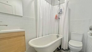 A bathroom with a freestanding bathtub, a toilet, and a shower curtain.