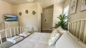 A bedroom with a bed, a TV, a dresser, and a door leading to another room.