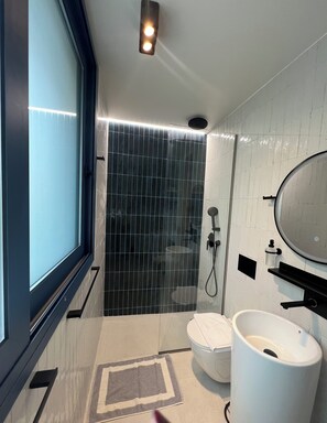 A modern bathroom with a large window, a shower with a black tile wall, a white sink, and a mirror. - SUGARBLUE-Minimal 1-bedroom villa with a spectacular seaview (Spartia)