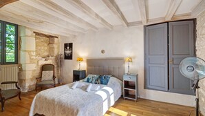 Ein Schlafzimmer mit Bett, Sessel, Nachttisch, Ventilator und Kleiderschrank.