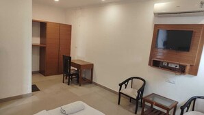 A hotel room with a bed, a desk, two chairs, a TV mounted on the wall, and a wardrobe. - Hotel Atlantiis Suites by Signature Stays (New Delhi)