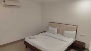 A bedroom with a bed, a nightstand, and an air conditioning unit on the wall. - Hotel Atlantiis Suites by Signature Stays (New Delhi)
