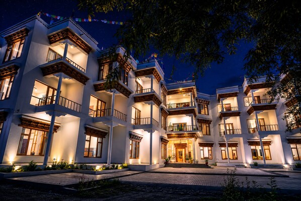 Un hotel de varios pisos con balcones, una entrada central y una fachada bien iluminada.