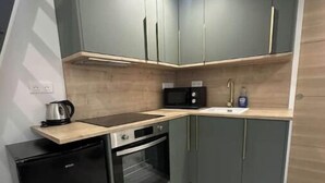 A compact kitchen with grey cabinets, a microwave, a sink, a stove, and a small refrigerator. - Self-contained studio near Paris (Vitry-sur-Seine)