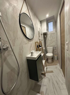 Un bagno stretto con doccia, WC e un piccolo angolo lavabo.
