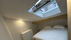 A bedroom with a skylight, a bed, a bedside dresser, and a wooden beam ceiling. - Self-contained studio near Paris (Vitry-sur-Seine)