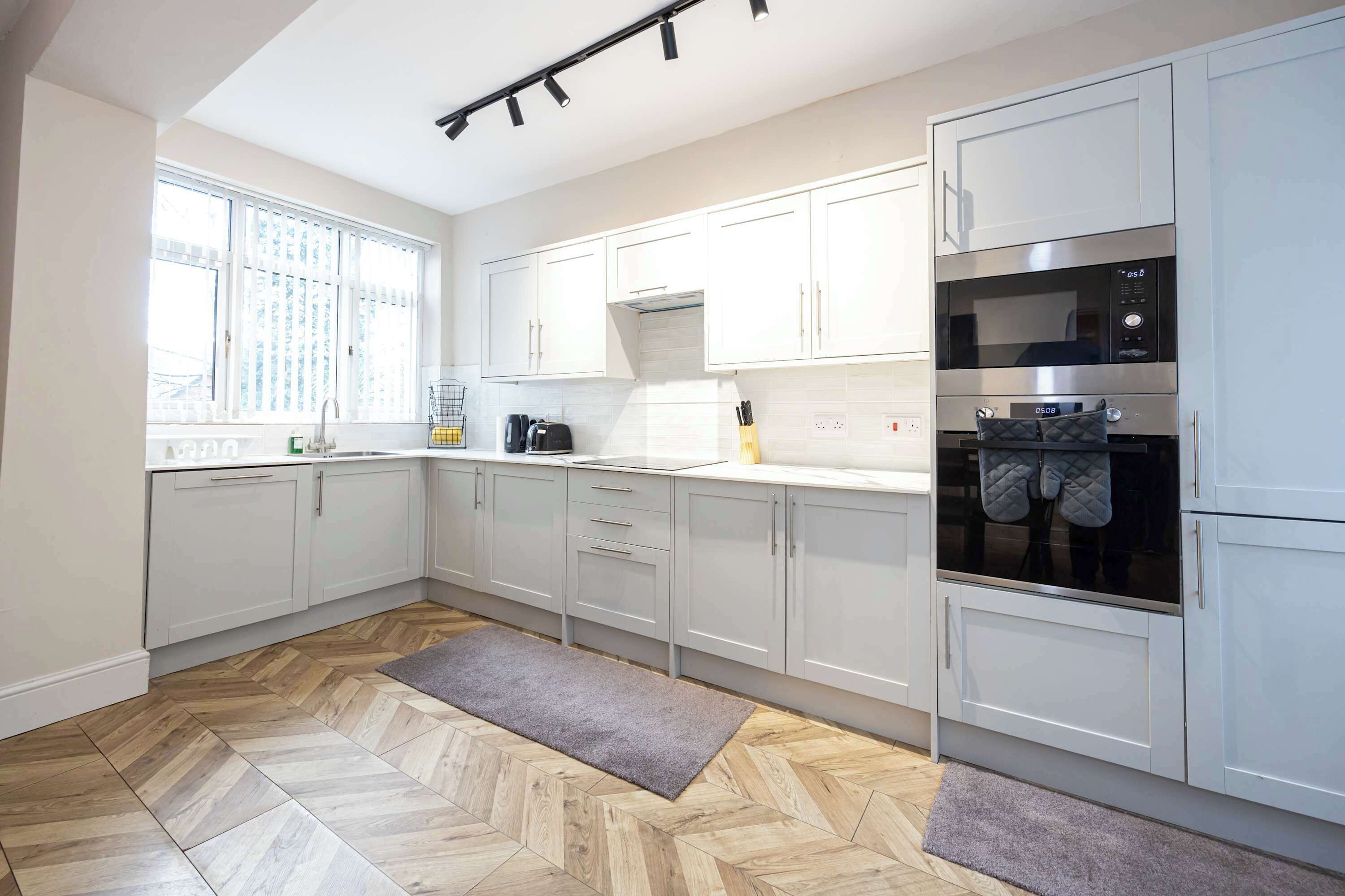 Eine moderne Küche mit weißen Schränken, einer Mikrowelle, einem Backofen und einem Fenster mit Jalousien.