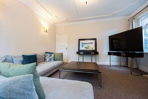 Ein Wohnzimmer mit einer Couch, einem Couchtisch, einem Fernseher und einem gerahmten Bild an der Wand.