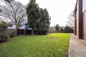 Ein Garten mit Rasenfläche, einer Backsteinmauer und einem großen Baum.