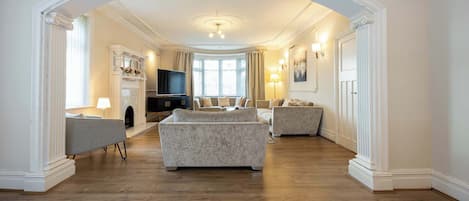 A spacious living room with a fireplace, a television, and a large window with curtains.