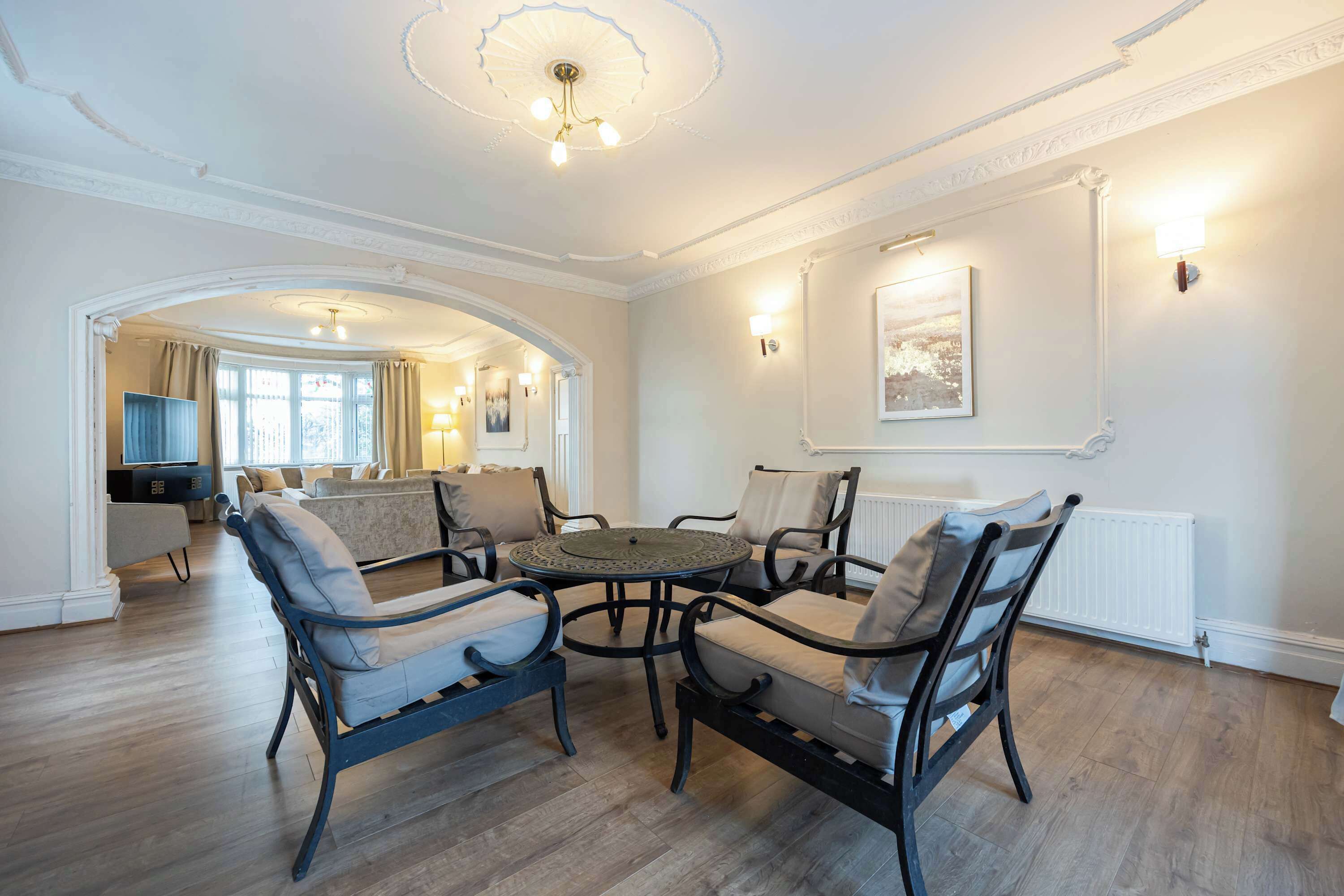 Een ruime woonkamer met een ronde salontafel, omringd door vier stoelen, een open haard en een stadsgezicht door grote ramen.