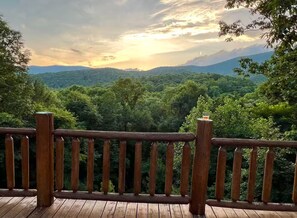 A wooden deck with a railing overlooking a forested landscape during sunset. - Entire cabin in Ellijay, Georgia (Ellijay)