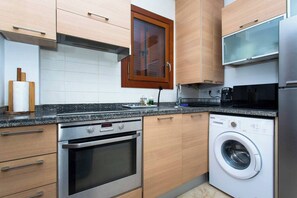 A modern kitchen with wooden cabinets, a stainless steel oven, a built-in washing machine, and a microwave.