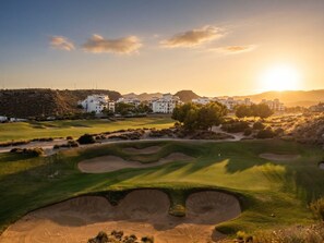 A golf course with bunkers, a clubhouse, and a sunset in the background. - Front Line Golf Luxury | Private Retreat & Course Views (Banos y Mendigo)