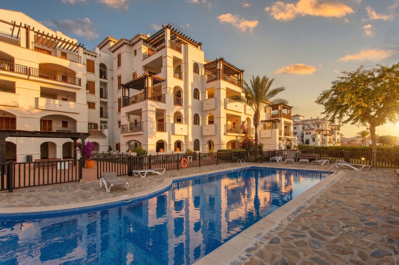 A hotel with a swimming pool, multiple balconies, and a stone-paved area.