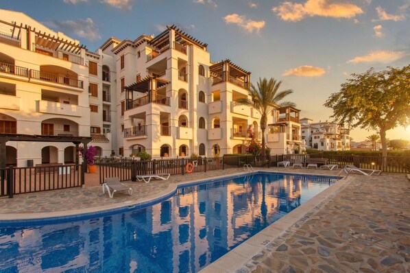 A hotel with a swimming pool, multiple balconies, and a stone-paved area.