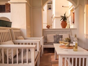 A sunlit outdoor seating area with white furniture, a table with wine glasses and a bottle, and a potted plant. - Front Line Golf Luxury | Private Retreat & Course Views (Banos y Mendigo)