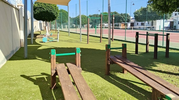 An outdoor playground with green artificial turf, wooden benches, and a shaded area.