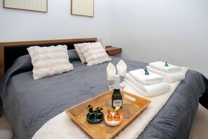 Een net opgemaakt bed met een grijze deken, twee witte kussens en een houten hoofdbord.