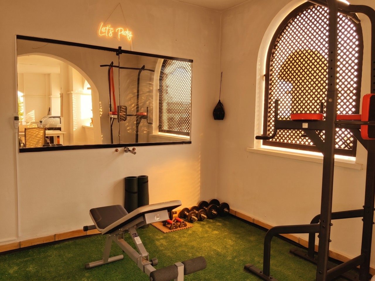 A home gym with exercise equipment, a mirror, and a window with a lattice design.