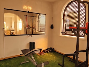A home gym with exercise equipment, a mirror, and a window with a lattice design.