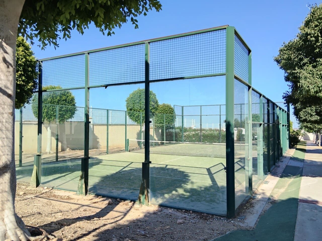 Una cancha de tenis rodeada por una cerca metálica verde y una red.