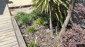 Een tuin met een houten terras, diverse planten en een stenen muur.