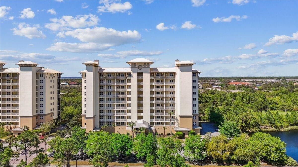 A multi-story hotel with a central tower and two side towers, surrounded by greenery and a body of water.