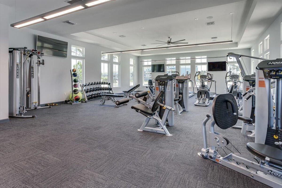 A modern gym with various exercise equipment, large windows, and a ceiling fan.