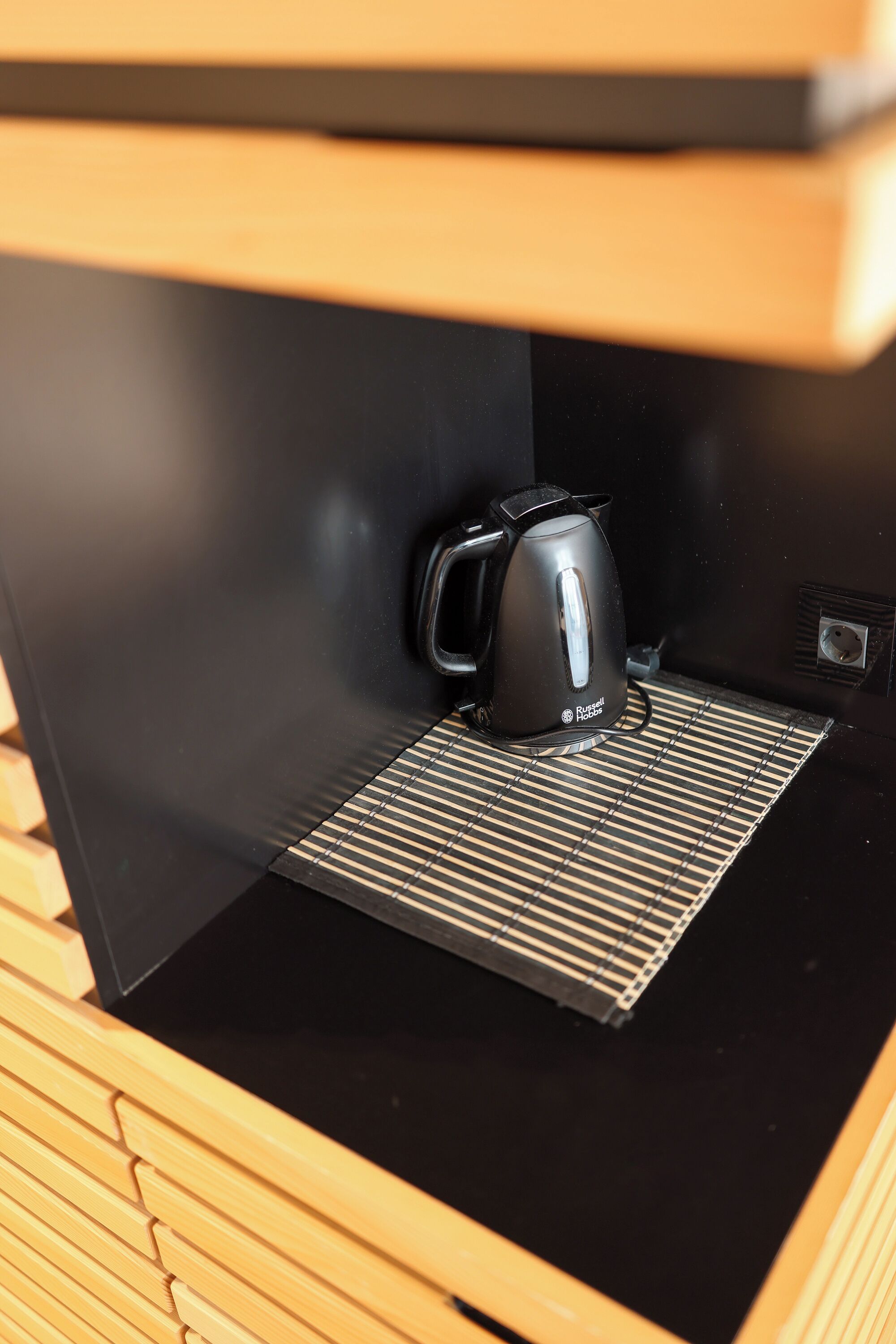 A black coffee maker on a black countertop with a metal grate underneath.