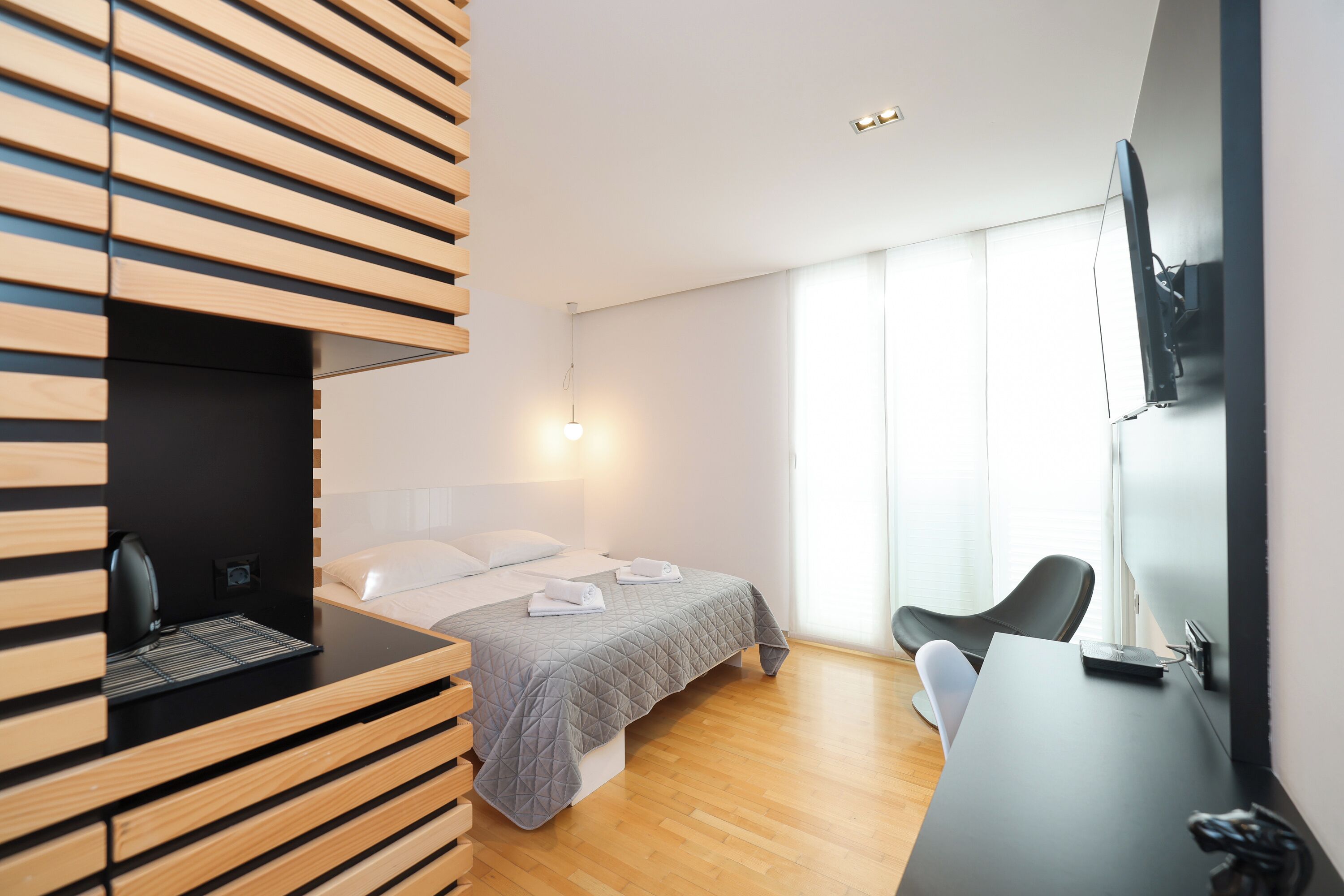Et moderne hotelværelse med seng, skrivebord, stol og fjernsyn monteret på væggen.