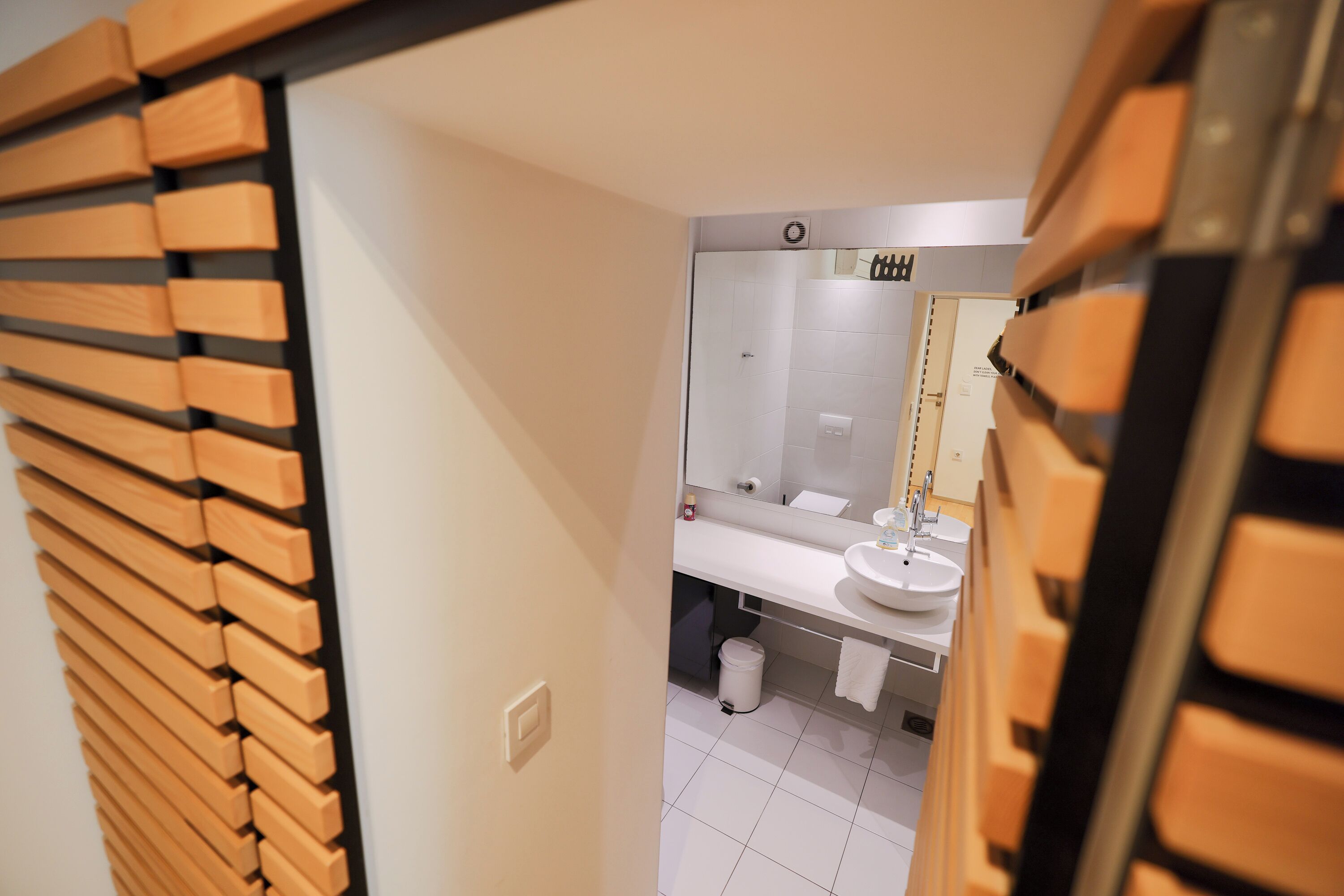 A modern bathroom with a wooden slat door, a white sink, and a mirror.