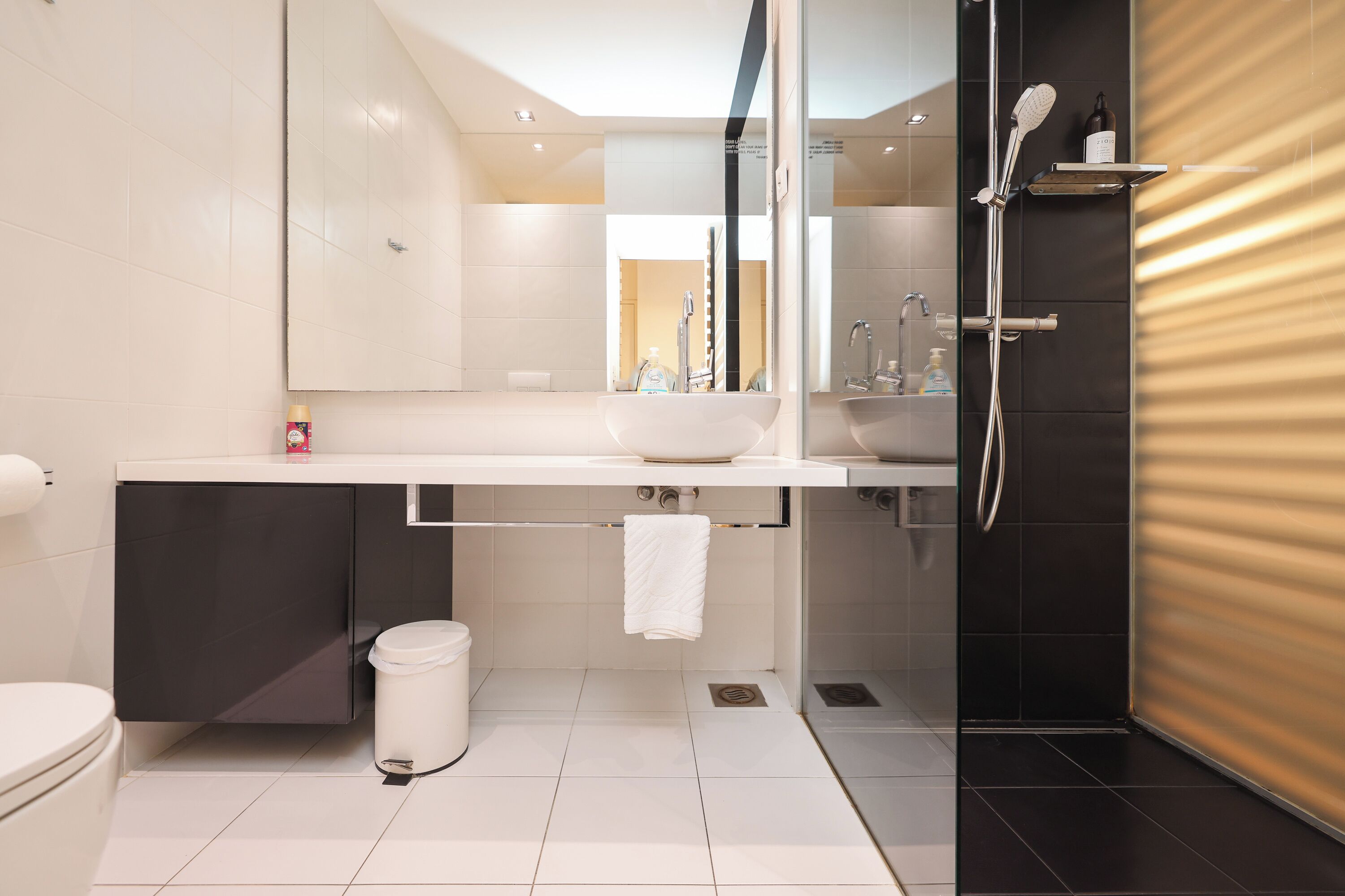 Un bagno moderno con lavandino bianco, uno specchio, una doccia e un water.