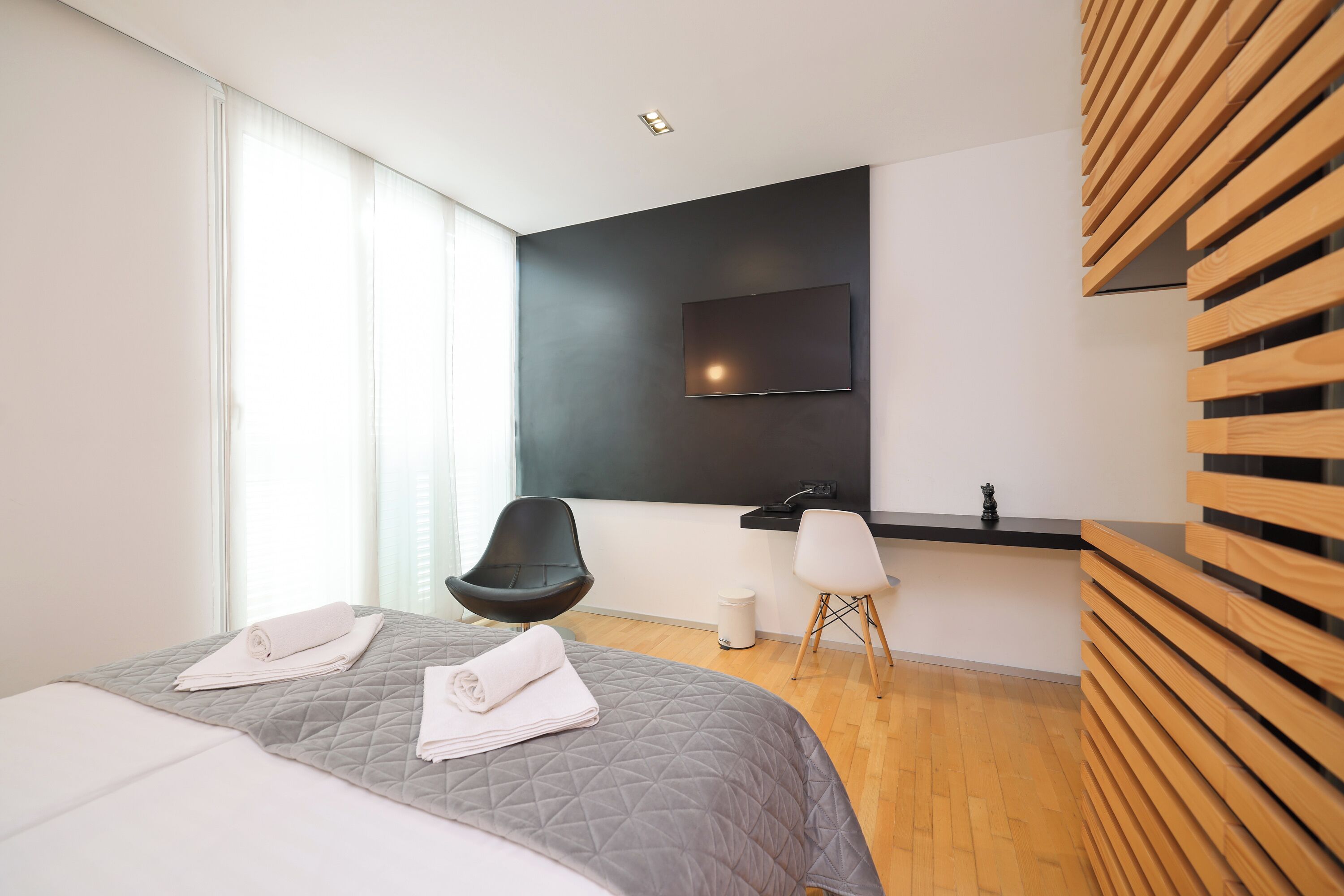 Una habitación de hotel moderna con una cama grande, un escritorio, una silla y un televisor fijado a la pared.