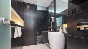 A modern bathroom with dark tiles, a white sink, and a glass shower enclosure.