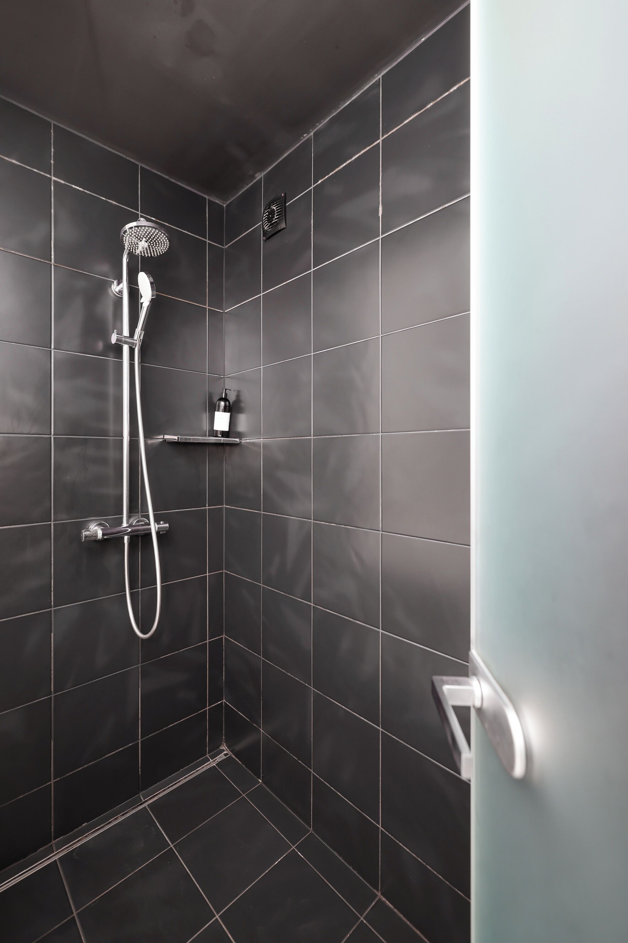 Une douche moderne dotée d’un pommeau de douche à main et d’un panneau de commande fixé au mur.