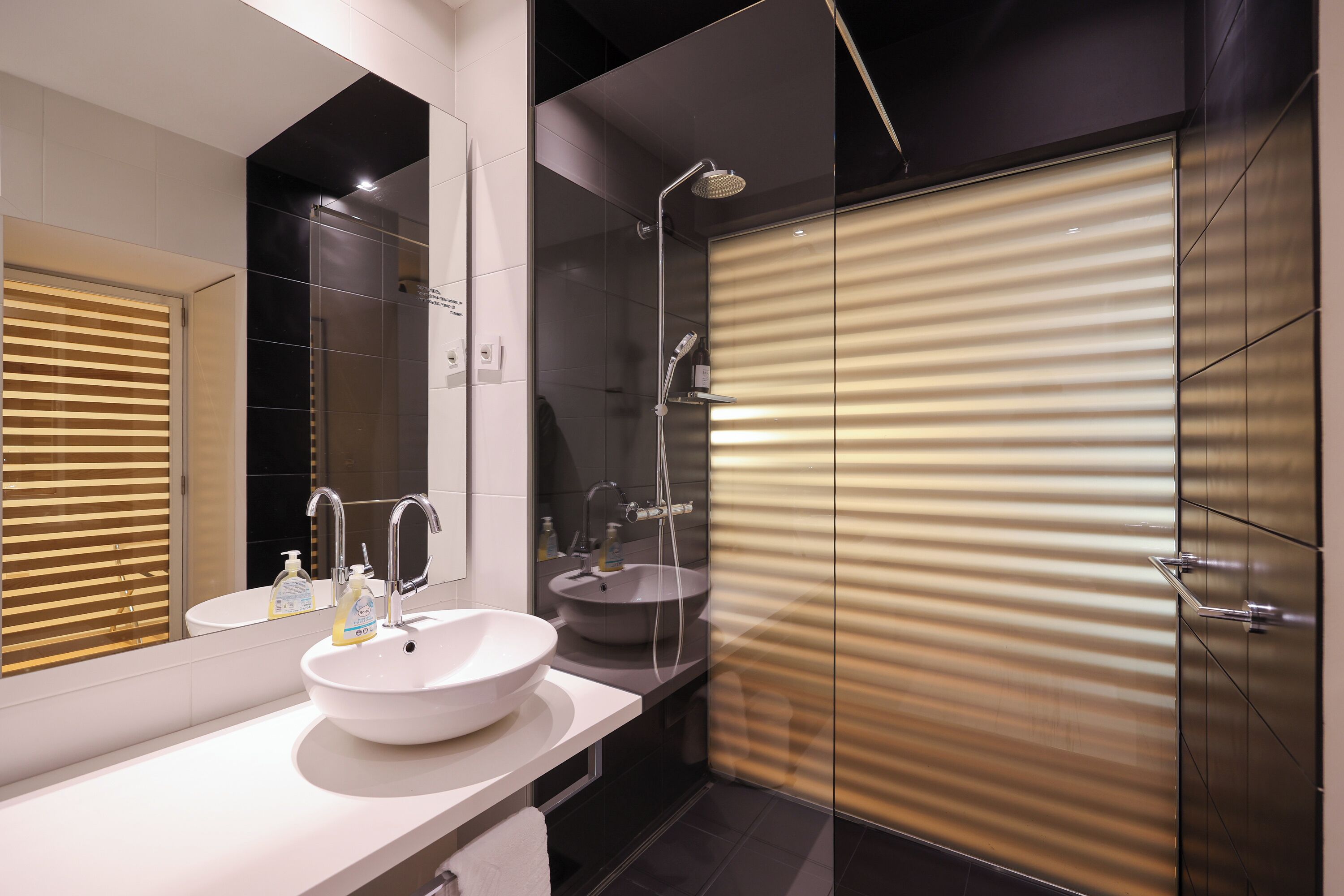 A modern bathroom with a white sink, a mirror, and a glass shower enclosure.