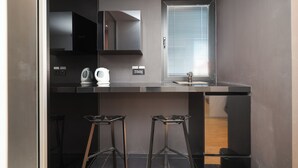 A modern kitchen with a black countertop, a window with blinds, and two black stools.