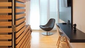 A modern living room with a wooden slatted wall, a black chair, a black sofa, a flat-screen TV mounted on the wall, and a wooden floor.