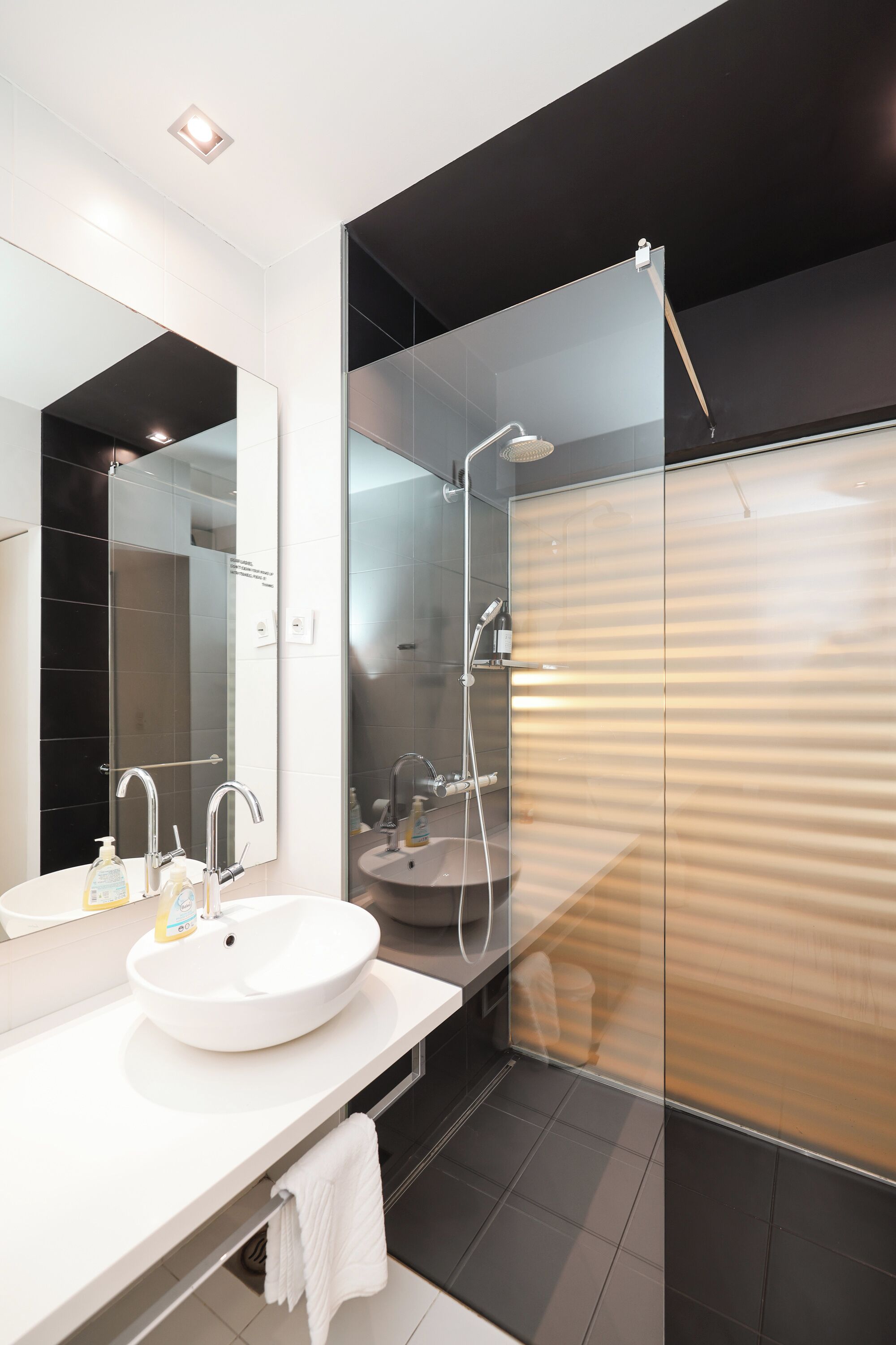Une salle de bain moderne avec un lavabo blanc, un grand miroir et une douche séparée par des parois en verre.