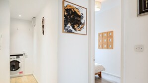 Uma lavanderia com máquina de lavar, um corredor com um quadro e um quarto com uma cama.