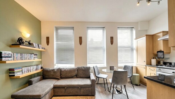 Uma sala de estar moderna com um sofá seccional, uma mesa de jantar com cadeiras, uma área de cozinha e estantes embutidas com livros.