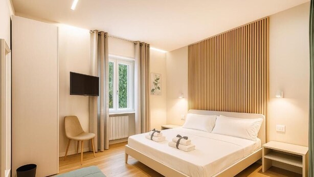 A modern bedroom with a bed, a chair, a TV, and a window with curtains. - Bergamoinluxe (Bergamo)