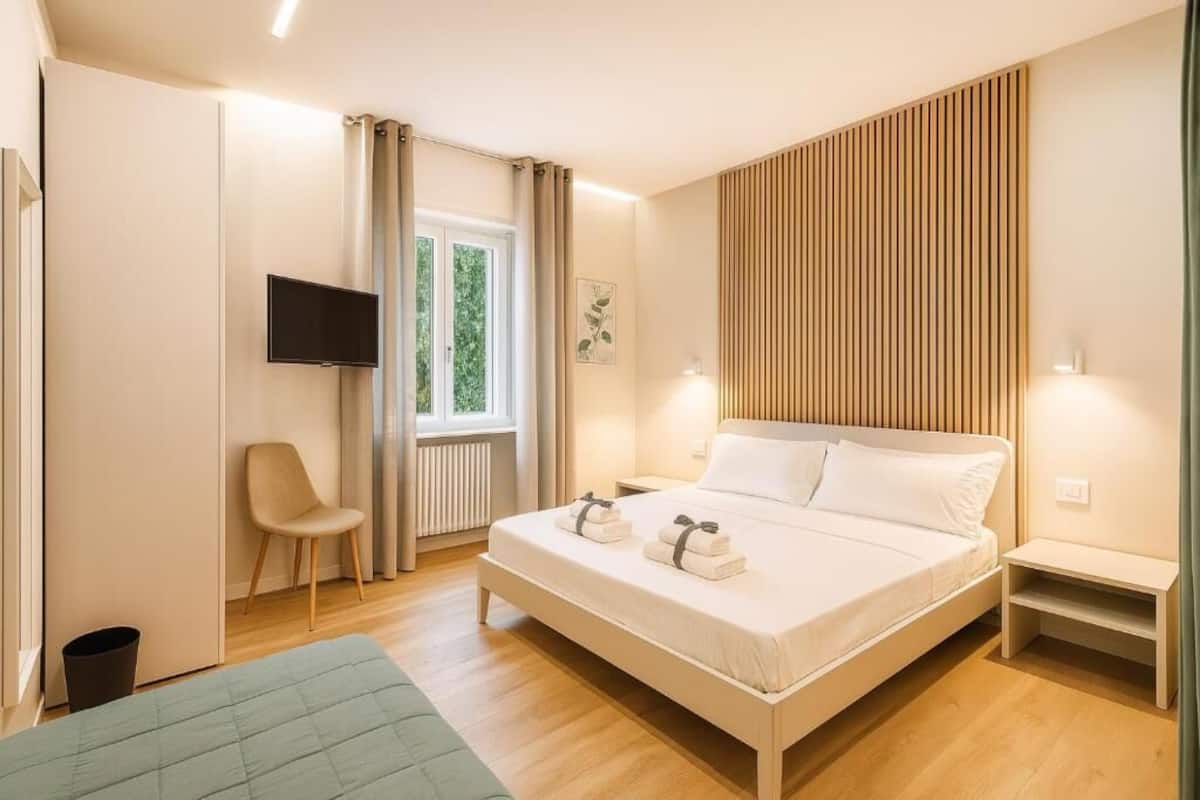 A modern bedroom with a bed, a chair, a TV, and a window with curtains.