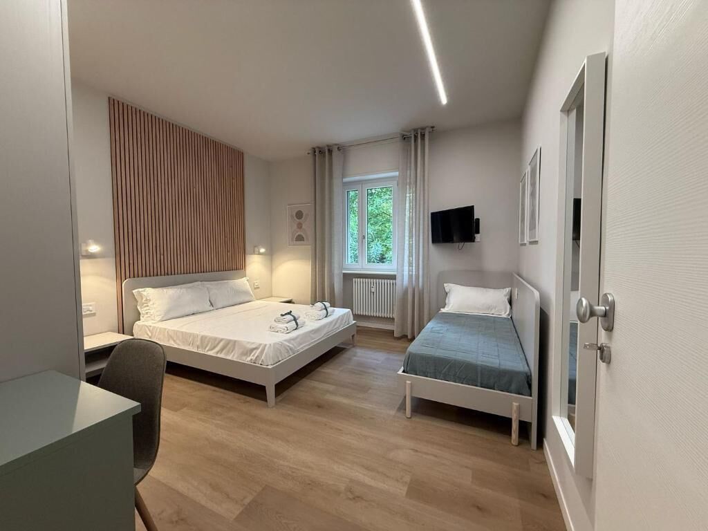 A bedroom with two beds, a desk, a chair, a TV, and a window with curtains.