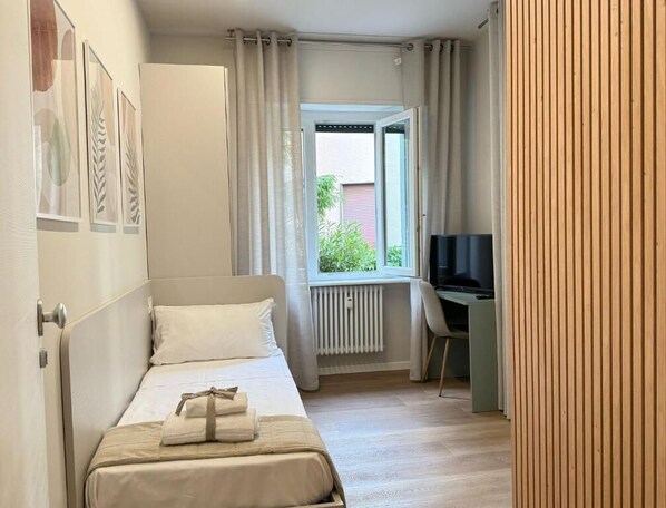 Ett sovrum med en säng, ett skrivbord, en tv och ett fönster med gardiner.