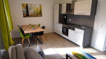 A modern kitchen with white cabinets, a wooden dining table, and a painting on the wall.