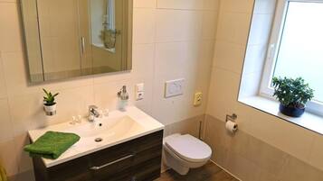 A bathroom with a white sink, dark wooden vanity, a toilet, and a window with a potted plant.