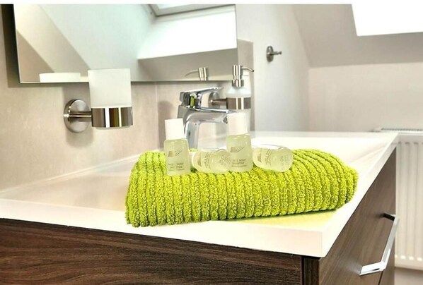 A bathroom with a modern sink, a mirror, and a green towel. - Pitlane Apartments by corents (Herresbach)