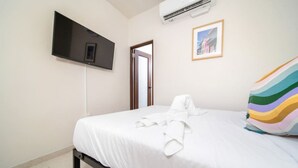 A hotel room with a bed, a TV mounted on the wall, an air conditioning unit, and a door leading to another room. - Vibrant Walkable Hub in Santurce (San Juan)